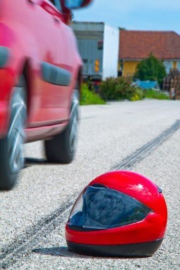 Motorcycle helmet next to skid marks on a road and a car