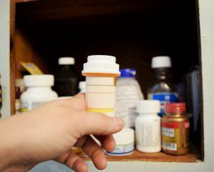 holding a prescription bottle in front of medicine cabinet