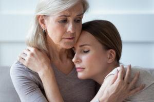 Gray-haired woman embracing a younger woman with sad and worried expressions