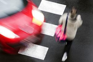 Blonde woman walking in a crosswalk with a red car speeding toward her.