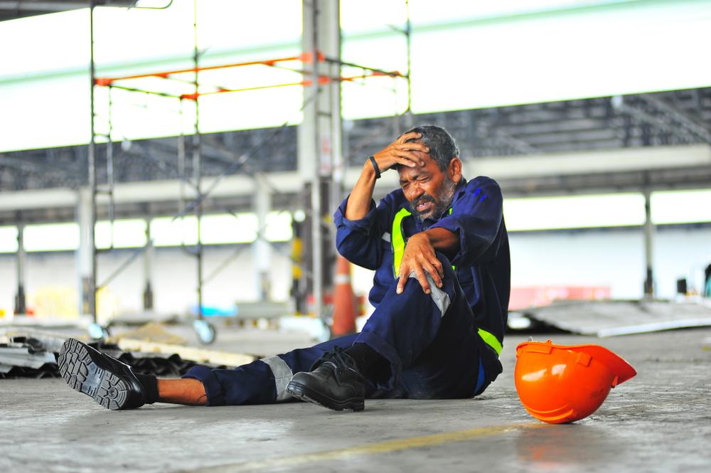 A man cringes with pain as he holds his injured knee in the workplace.