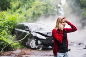 A distressed woman talks on the phone in front of a car crash.