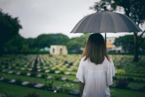 a young woman holding a black umbrella at a gravesite