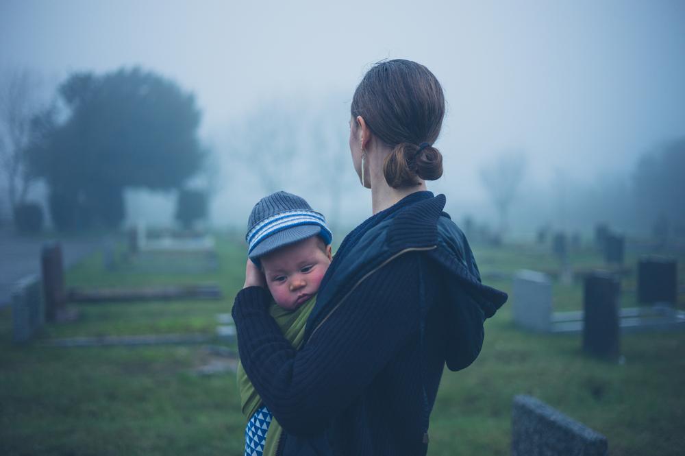 grieving mother with her young baby in a graveyard