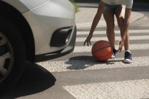 teenager grabbing a basketball in a crosswalk as a car approaches