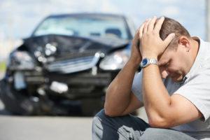 upset driver sits near his damaged vehicle
