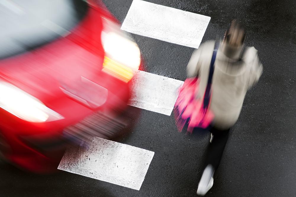 A woman walking in a crosswalk in front of a moving red car