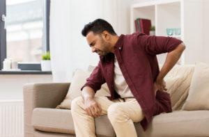 man with back pain sitting on the couch