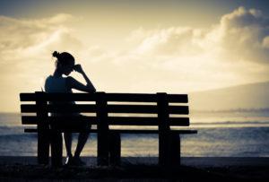 grieving woman sits on bench at sunset